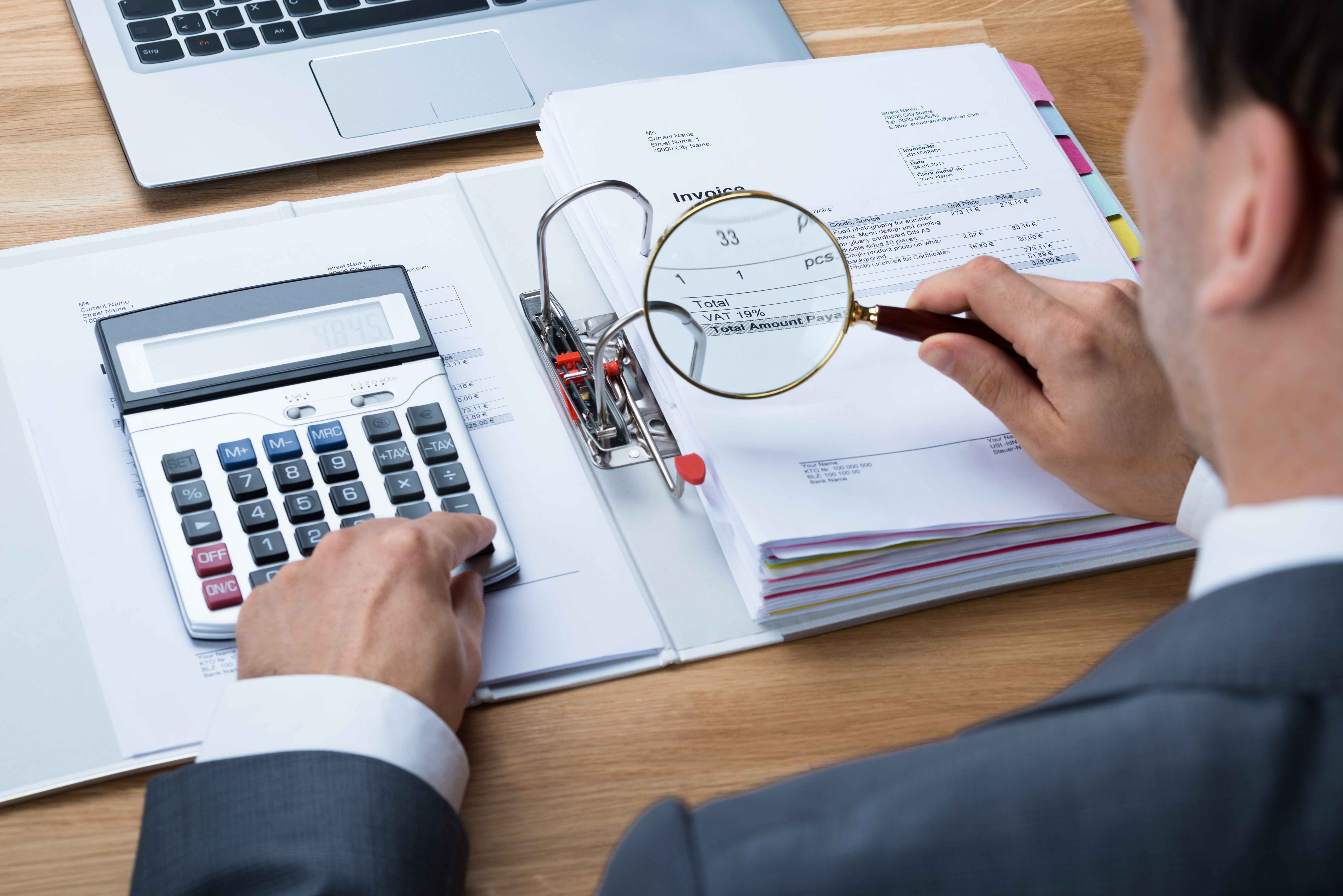 Professional accountant analyzing financial documents with calculator and magnifying glass on wooden desk
